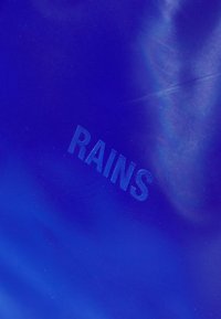 Royal blue waterproof material with a smooth texture, featuring the embossed word "RAINS" near the bottom. Minimal design, no additional accents.