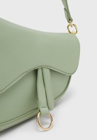 Borsa in pelle verde testurizzata con una patta curva, accessori in oro e una tracolla a goccia. Presenta una silhouette liscia e distintiva.