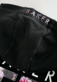 Čierna mikina s kapucňou s jemnou textúrou, s nášivkou s kvetinovým vzorom a slovom "BAKER" v iridescentnom písmene na chrbte.