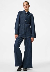 Conjunto de denim con rayas verticales blancas; camisa de botones de manga larga y pantalones de pierna ancha. Color azul oscuro, textura suave y estilo ajustado.