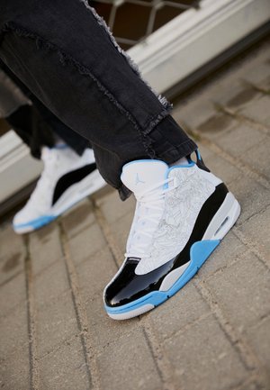 Witte en zwarte sneakers met blauwe accenten, voorzien van complexe patronen aan de zijkant, een glanzende zwarte neuskap en textiel stof.