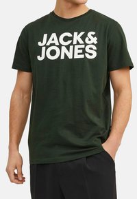 Dark green cotton t-shirt featuring large white text "JACK & JONES" on the front. Short sleeves and a crew neckline. Soft texture.