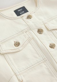 Veste en denim beige à boutons, avec deux poches à rabat et des boutons beiges, étiquetée "NEXT Fuller Bust".
