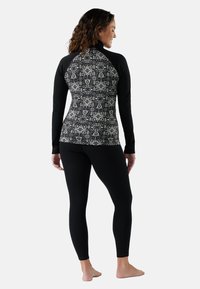 Maglietta a maniche lunghe nera con un motivo geometrico sulla schiena, abbinata a leggings neri. Tessuto morbido e design aderente.