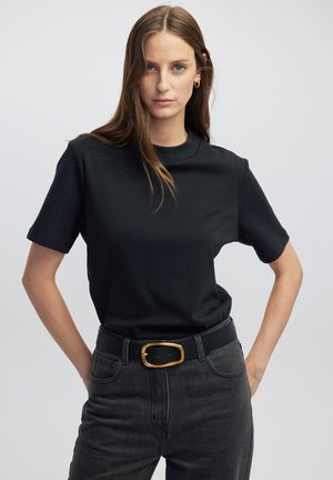 Camiseta de algodón negra de mangas cortas, con cuello redondo, combinada con unos jeans gris oscuro y un cinturón negro con una hebilla rectangular dorada.