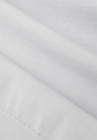 Biała bawełniana tkanina o gładkiej fakturze, pokazująca drobny splot i subtelne rozciągnięcie, złożona tak, aby ukazać warstwowe powierzchnie i szczegóły szwów.