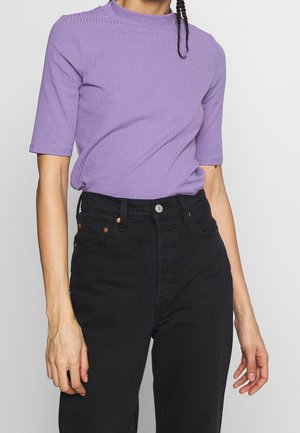 Haut court à manches courtes côtelé lilas avec un col montant, associé à un jean noir taille haute avec des garnitures et des poches couleur cuivre.