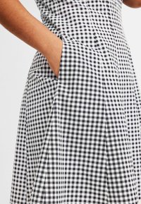 Zwart-wit gingham jurk met een aansluitende lijfje, volle rok en zijzakken. De stof is lichtgewicht met een zachte textuur.