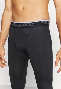 Czarne legginsy sportowe wykonane z elastycznego materiału, z szerokim pasem Nike Pro z kontrastowym logo i dopasowanym krojem.