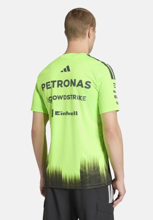 Homme portant un maillot de sport vert vif avec un dégradé noir en bas et des logos de sponsors (Petronas, CrowdStrike, Einhell) au dos.