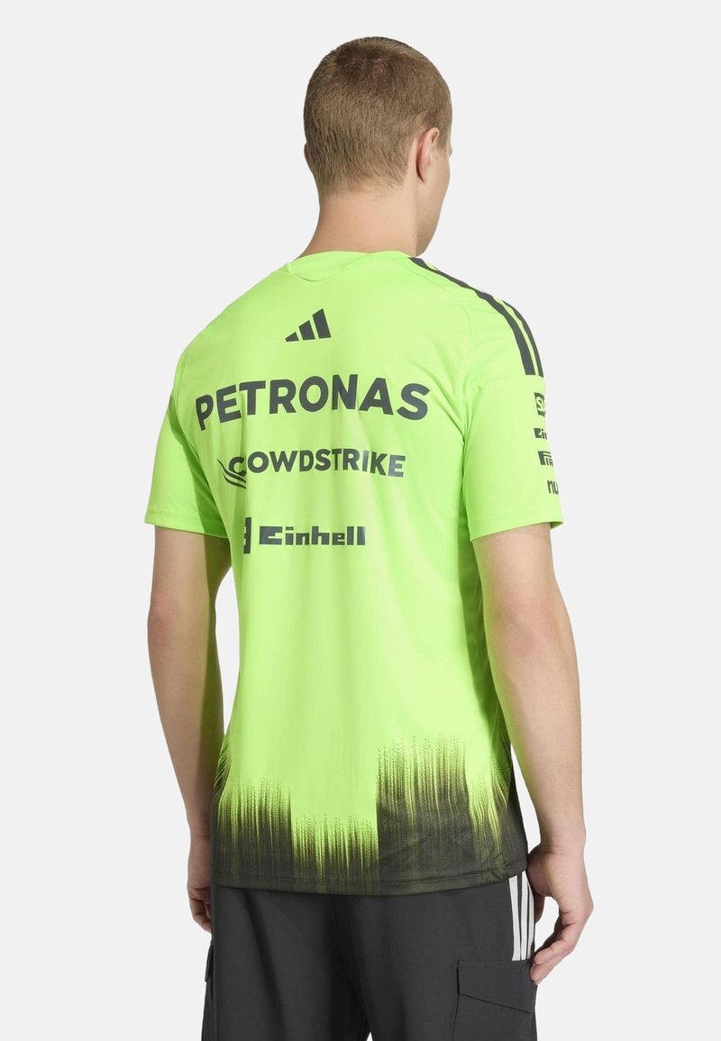 Homme portant un maillot de sport vert vif avec un dégradé noir en bas et des logos de sponsors (Petronas, CrowdStrike, Einhell) au dos.