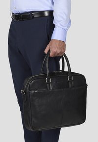 Sort læder laptop taske med to håndtag, rektangulær form, glat tekstur, sølv hardware detaljer og lynlås lukning.