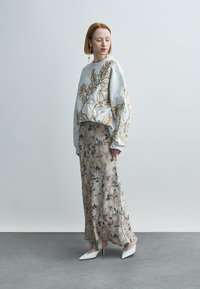 Ανοιχτό γκρι φούτερ με χρυστή κεντητή λουλουδάτη διακόσμηση, σε συνδυασμό με μακριά, μπεζ φούστα με σχέδια λουλουδιών. Λευκά ψηλοτάκουνα παπούτσια.