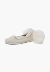 Beige ballet flat with a textured surface, featuring a decorative bow made of sheer fabric on the side, displayed on a white background.