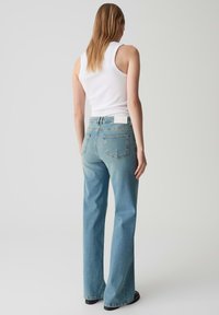 Jeans a zampa d'elefante blu chiaro con una texture sbiadita, caratterizzati da due tasche posteriori e un'etichetta bianca sulla vita. Abbinati a una canotta bianca.