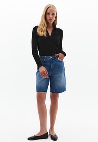 Schwarzes Langarmshirt, hoch geschnittene blaue Jeansshorts mit ausgefranstem Saum und schwarze Ballerinas. Einfaches Design und klassische Farben.