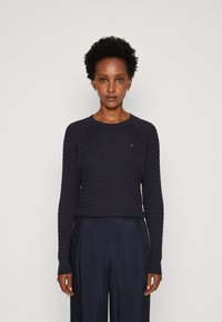 Maglione lavorato a maglia blu navy con un motivo testurizzato, scollo rotondo e maniche lunghe. Presenta polsini a coste e un piccolo dettaglio con logo.