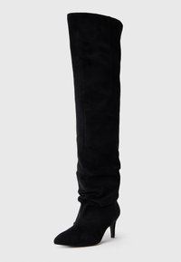 Botas negras de ante hasta la rodilla, con punta afilada, diseño elástico y un tacón delgado y medio. Textura suave y mate.