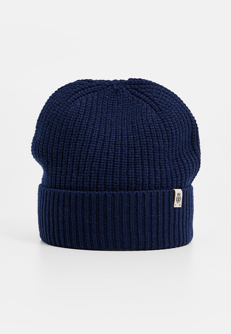 Granatowa prążkowana dzianinowa czapka z wywiniętym mankietem i małą beżową metką z czarnym emblematem po boku.