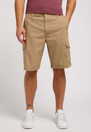 Shorts cargo caqui con bolsillos laterales, fabricados con un tejido duradero, cuentan con un ajuste relajado y dobladillo cosido. Combinados con zapatillas blancas.
