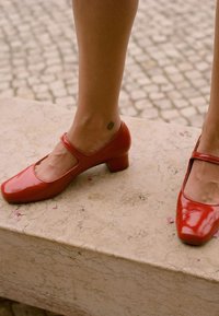 Czerwone lakierowane buty na niskim obcasie z kwadratowym noskiem, z wycięciami i cienkim paskiem na wierzchu stopy.