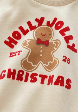 Kermainen collegepaita, jossa on piparkakkumiehen grafiikka punaisella solmiolla, ympäröitynä punaisella tekstillä "HOLLY JOLLY CHRISTMAS EST 25."