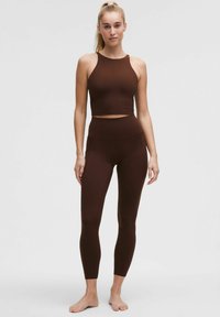 Pruun spordikropp ja kõrge talje ning venivast kangast leggings, millel on vormitud disain ja sile tekstuur.