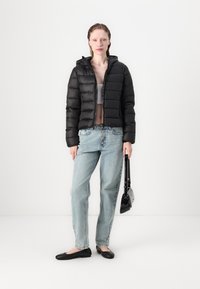 Černá péřová bunda s kapucí, prošívaný design, přední zip. V kombinaci s světlými modrými volnými džíny, černými plochými botami a malou černou taškou.