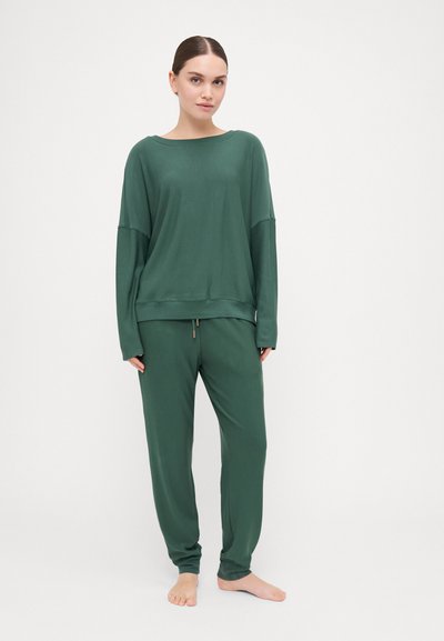 Conjunto de roupa de estar verde, composto por uma blusa de manga longa de corte solto e calças afuniladas, confeccionado em material macio com um brilho subtil.