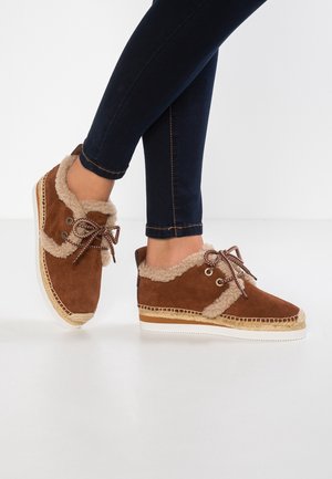 Brown suede sneakers with faux fur lining, featuring a rounded toe, lace-up design, and espadrille-style jute detailing on the sole.