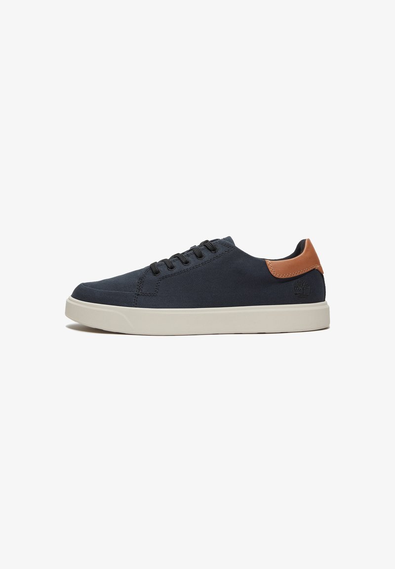 Zapatilla de lona navy con cordones negros y un acento de cuero marrón claro en el talón. Cuenta con una suela de goma blanca y detalles de costura simples.