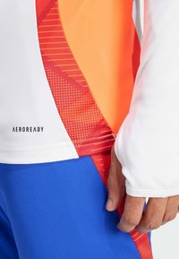 Sportliches T-Shirt mit kurzen Ärmeln in einem weißen, orangefarbenen und roten Farbschema mit einem strukturierten Muster. "AEROREADY"-Logo nahe dem Saum.