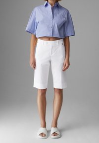 Zkrácená světle modrá košile s krátkým rukávem, bílé upravené šortky a bílé nazouvací sandály. Košile má oranžový šňůrkový detail.