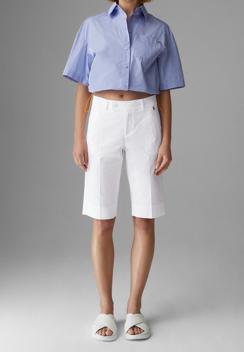 Zkrácená světle modrá košile s krátkým rukávem, bílé upravené šortky a bílé nazouvací sandály. Košile má oranžový šňůrkový detail.