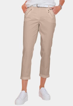 Beige Cropped-Hosen mit umgeschlagenen Säumen, zwei schrägen Fronttaschen mit Reißverschlüssen, kombiniert mit weißen Plateauschuhen. Einfaches Design und glatte Textur.