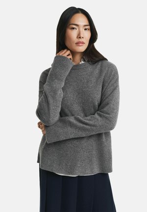Maglione grigio lavorato a maglia con maniche lunghe, scollatura rotonda e orlo a coste. Il materiale sembra morbido e testurizzato, adatto per il tempo fresco.