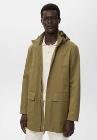Chaqueta verde oliva de longitud media con capucha, cremallera en la parte delantera y dos grandes bolsillos frontales; textura suave y diseño minimalista.