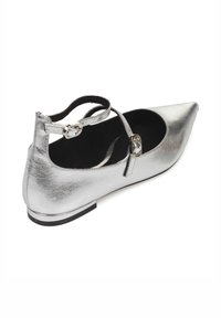 Zapato plano metálico plateado con punta afilada, tira en el tobillo y hebilla decorativa. Textura suave con un diseño minimalista y suela negra.