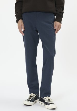 Navyblaues Hosen mit glatter Textur, geradem Schnitt und Fronttaschen, kombiniert mit schwarzen Sneakers mit weißen Sohlen und Schnürsenkeln.