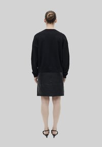 Maglione nero oversize con spalle abbassate abbinato a una gonna di pelle nera a lunghezza ginocchio. Indossato da un modello che indossa tacchi a punta neri, visto da dietro.