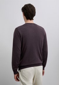 Donkerpaarse trui met lange mouwen, een ronde halslijn en geribbelde manchetten; gedragen met lichtgekleurde broek. Zachte textuur en casual pasvorm.