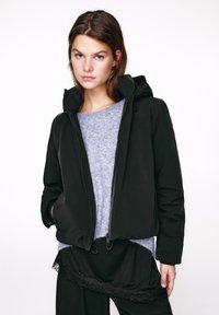 Čierna bunda s kapucňou a predným zipsom, s elastickými manžetami a hladkou textúrou, nosená cez svetlosivý sveter s jemným povrchom.