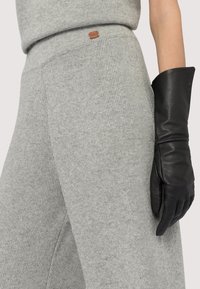 Szary sweter dziewiarski z teksturowanym wykończeniem. W połączeniu z dopasowaną czarną skórzaną rękawiczką, podkreślającą kontrast materiałów.