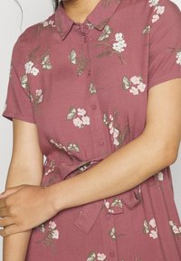 Sukienka z krótkim rękawem w mauve z floralnym i motylkowym wzorem, z zapięciem na guziki z przodu oraz wiązaniem w talii. Gładka tekstura, lekka kompozycja.