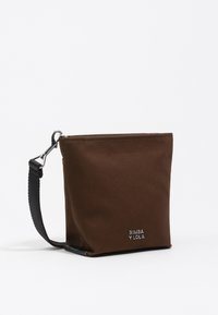 Pochette in materiale sintetico marrone con superficie texture, hardware argentato e una tracolla in tessuto nero. Marchio ben visibile nella parte inferiore.