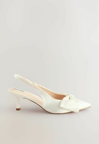 Valkoiset slingback-kengät, joissa on teräväkärkinen muotoilu, edessä kauniit nauhat yksityiskohtina ja kapea, neliömäinen korko. Tasainen nahkapinta.