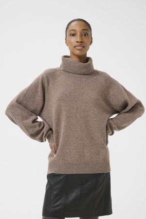 Brown, oversized knitted sweater with a high collar, raglan sleeves, and a ribbed hem. Worn over a black leather skirt.