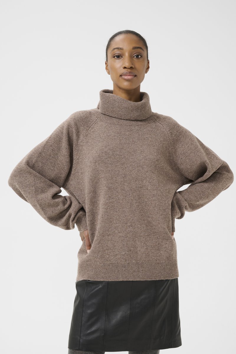 Brown, oversized knitted sweater with a high collar, raglan sleeves, and a ribbed hem. Worn over a black leather skirt.
