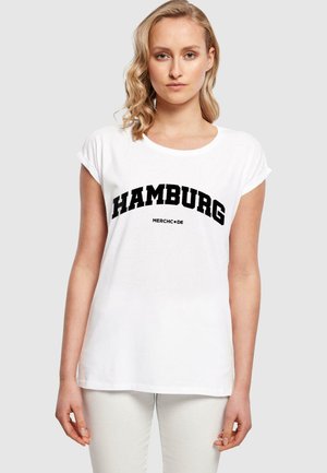 Hvit t-skjorte med "HAMBURG" i fet svart skrift. Rund hals, korte rullede ermer, mykt bomullsmateriale, avslappet passform.