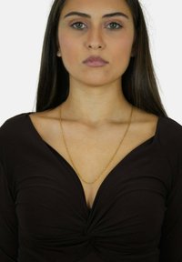 Top marrone con scollatura a V e design frontale attorcigliato. Una delicata collana d'oro completa l'outfit.